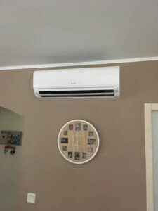 Module intérieur d'une climatisation réversible posée contre un mur marron, au-dessus d'une horloge bois.